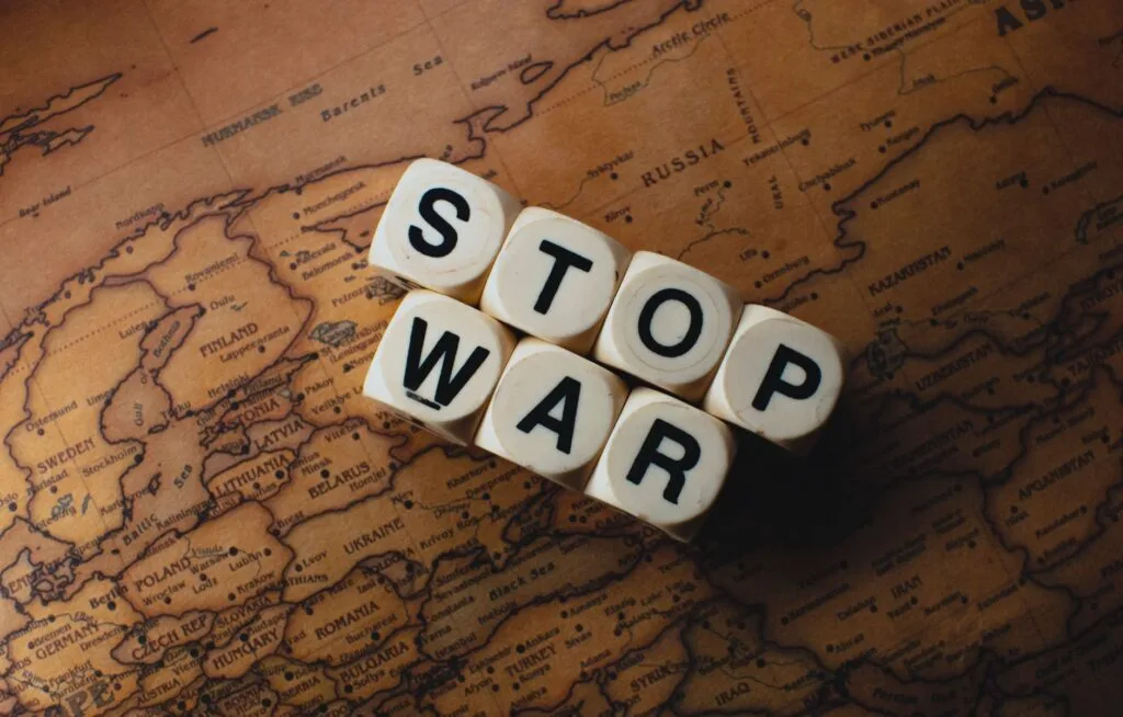 Dadi bianchi con le lettere S, T, O, P, W, A, R disposti su una mappa antica del mondo per formare il messaggio "STOP WAR".